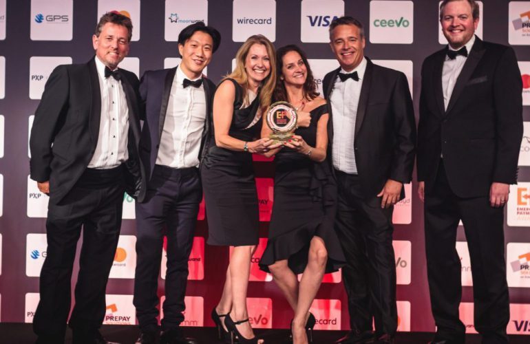 Group of professionals in formal attire holding an award on stage at an industry awards event.